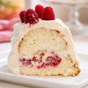 Homemade Raspberry And Cream Angel Food Cake topped with fresh whipped cream and berries.