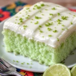 Slice of Green Cake with Key Lime Icing garnished with lime zest on a white plate.