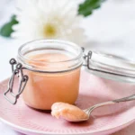 A jar of easy rhubarb curd spread on toast with rhubarb slices in the background